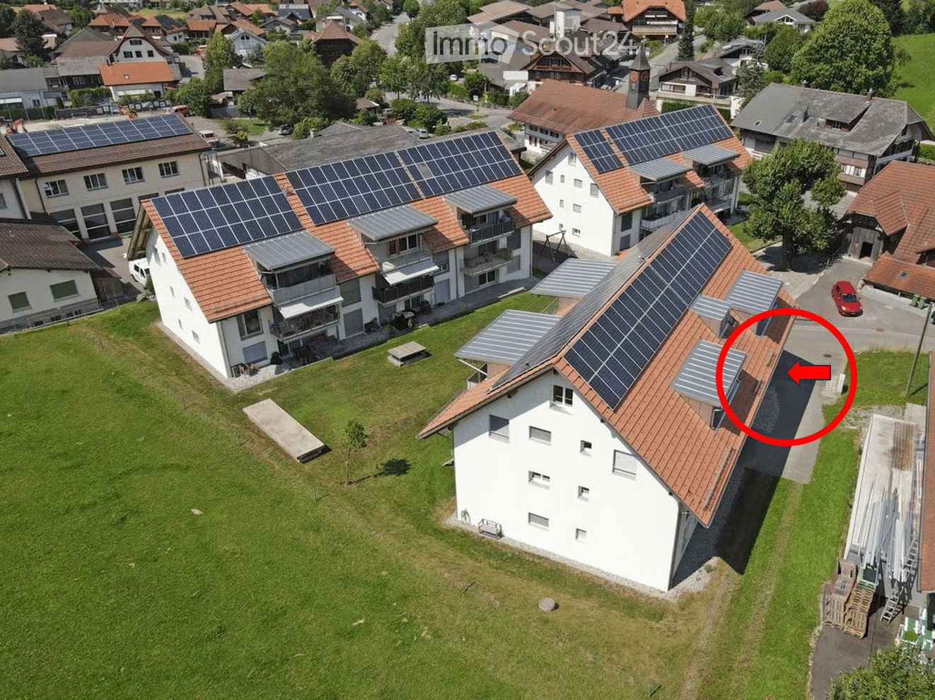 Aerial view of a residential area with multiple houses, solar panels on roofs, and a well-maintained lawn.
