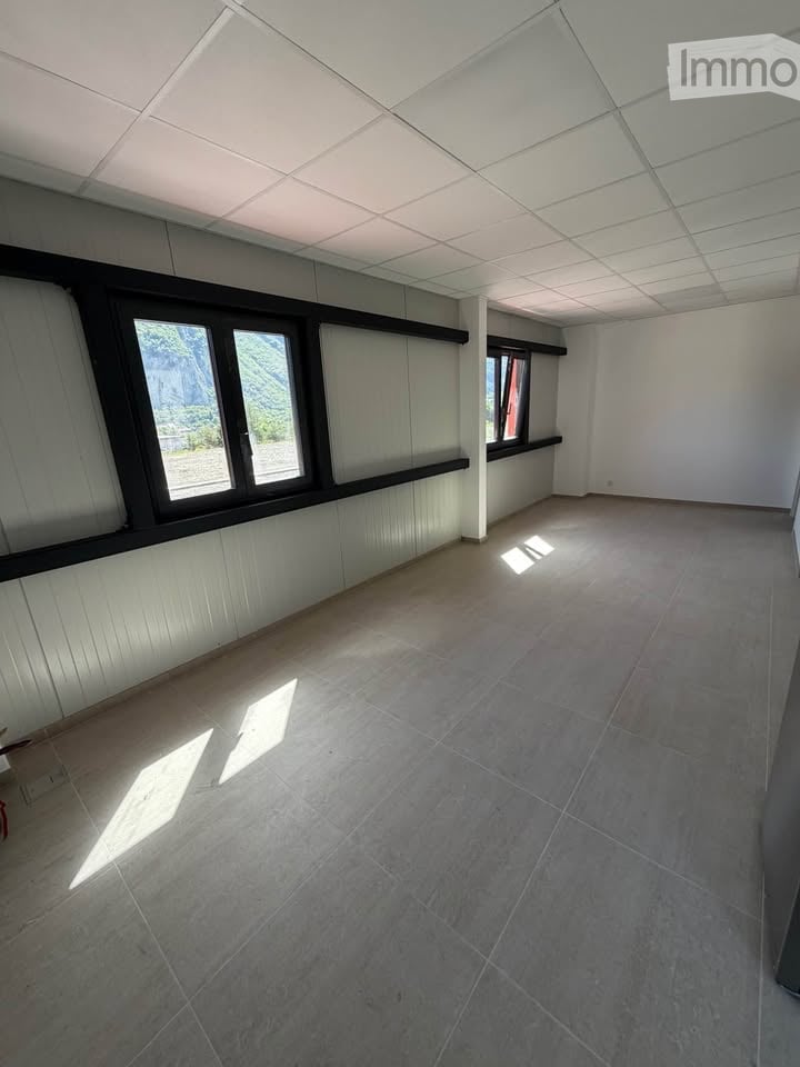 Empty room with grey tiled floor, white walls, and large windows with black frames. No furniture or equipment present.