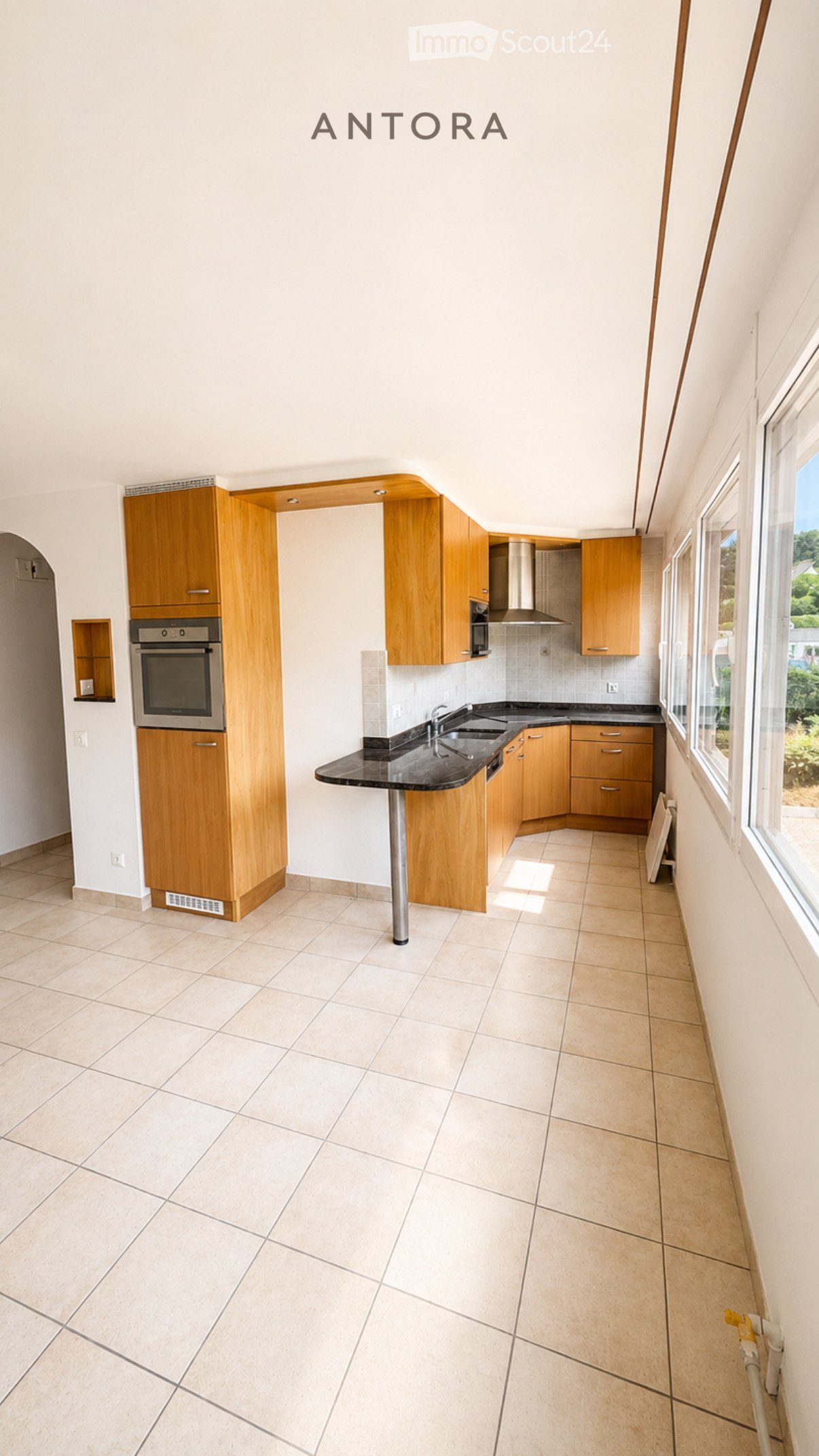 Modern kitchen with light wooden cabinets, stainless steel oven, black countertop, and tiled floor.