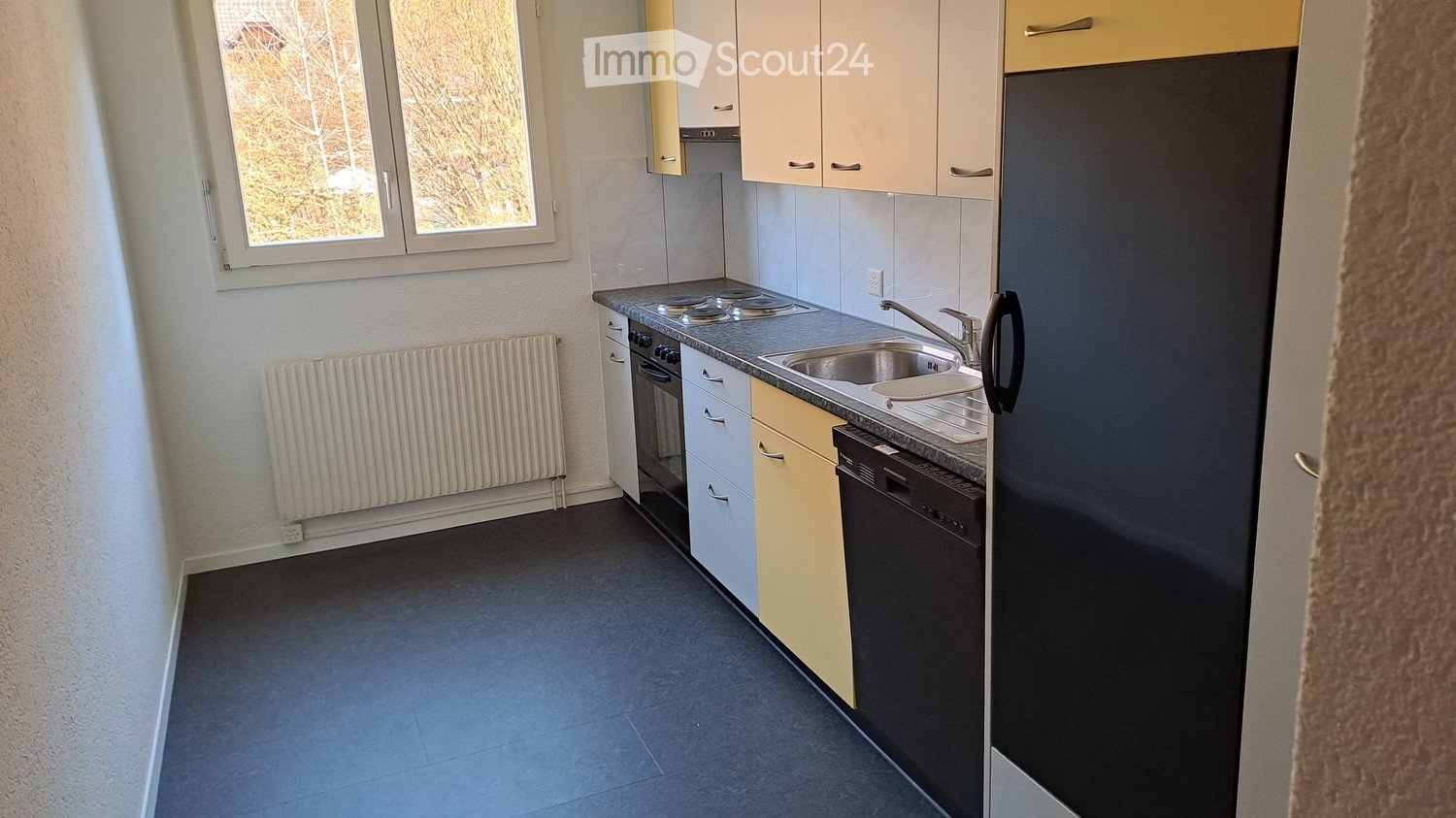 Compact kitchen with window, tiled floor, white cabinets, sink, oven, refrigerator
