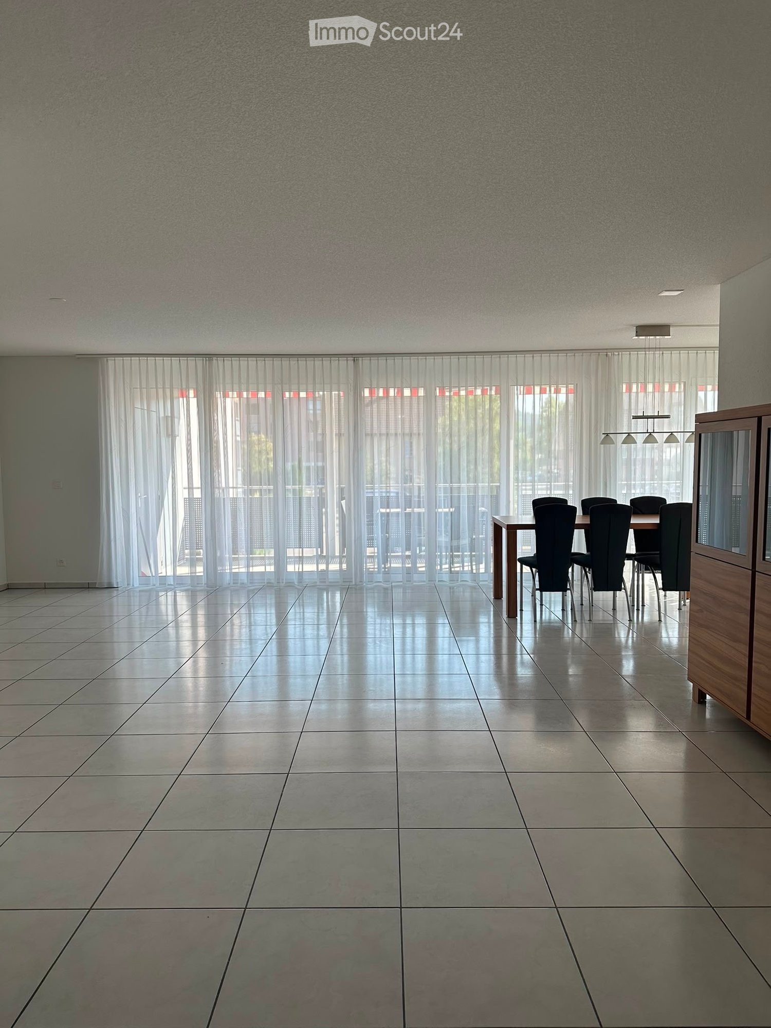 Dining room with tiled floor, large windows with sheer curtains, and a dining table with chairs.