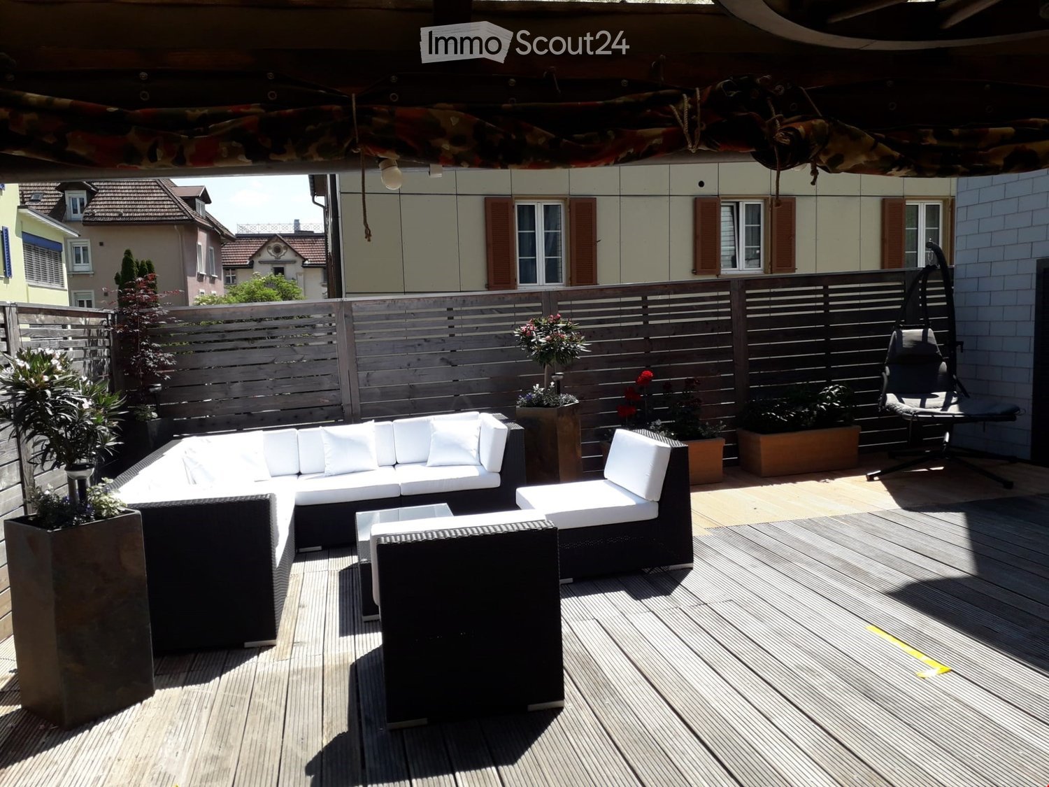 Wooden deck with white outdoor sofa, matching chairs, small table, and potted plants.