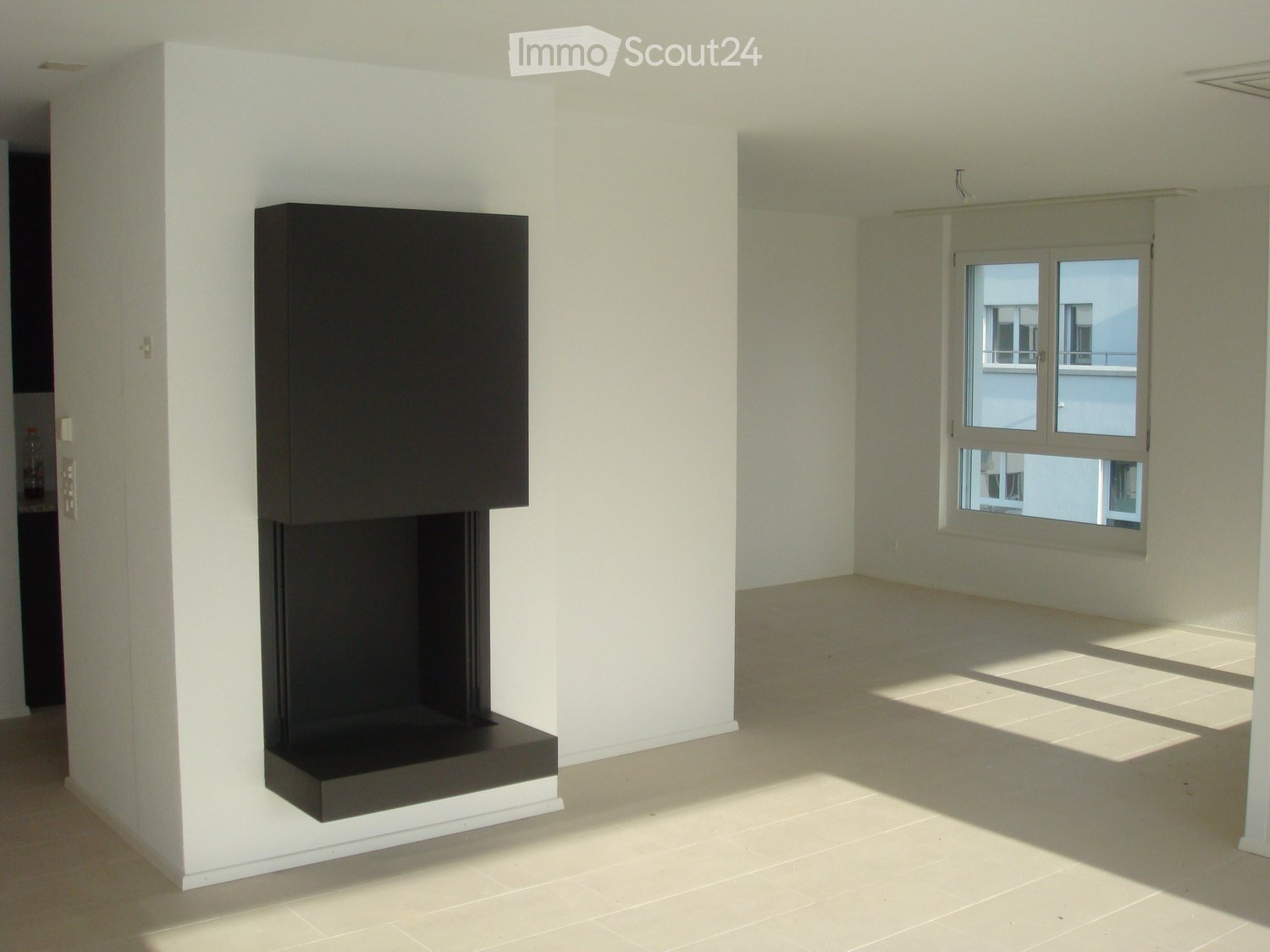 Empty room with white walls, tiled floor, and a built-in fireplace. A window with a view of another building is visible on the right side.