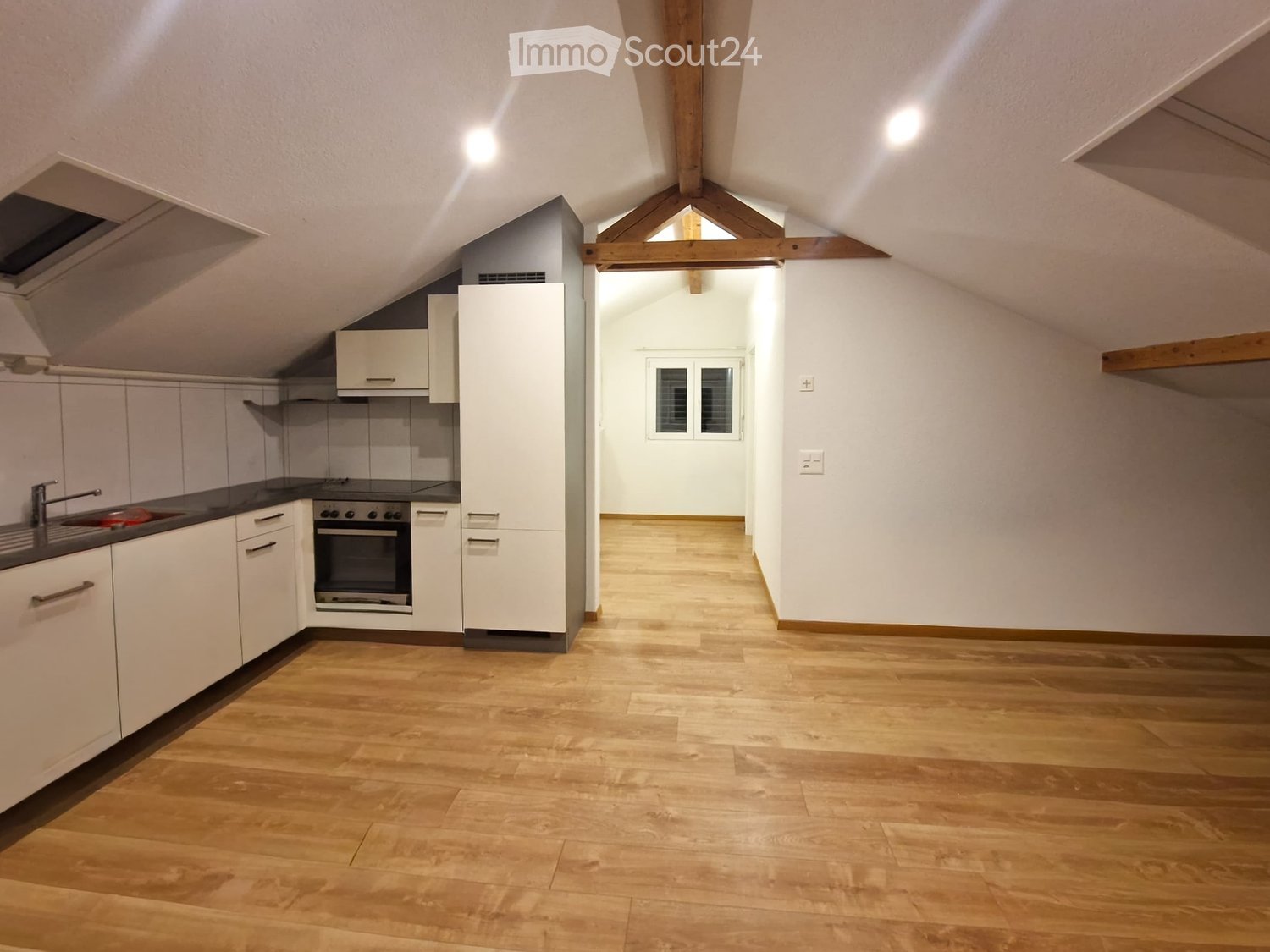 empty attic kitchen with white cabinets, wooden floors, wooden beams, kitchen appliances, white ceilings