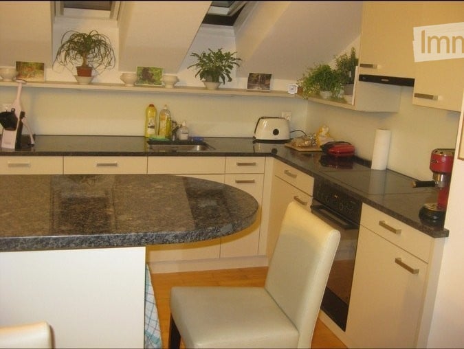 Modern kitchen with white cabinets, granite countertop, built-in appliances, and a white chair near the island.