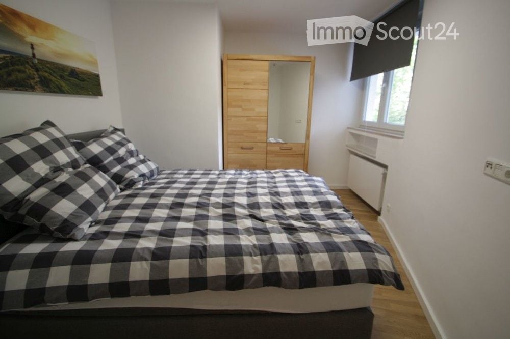 Cozy bedroom with a wooden bed, checkered bedding, a wooden wardrobe with a mirror, and a landscape painting on the wall.