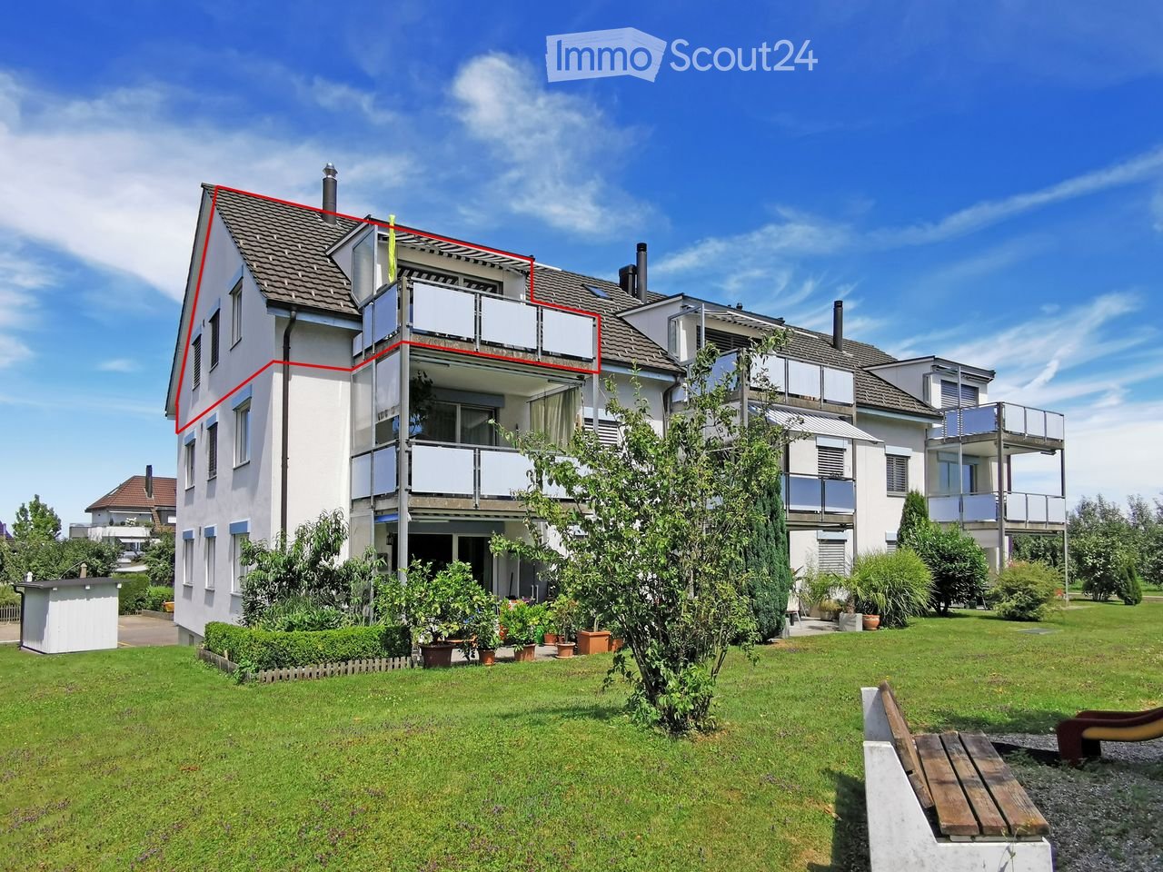Modern multi-story residential building with balconies, surrounded by a well-maintained lawn and garden area.