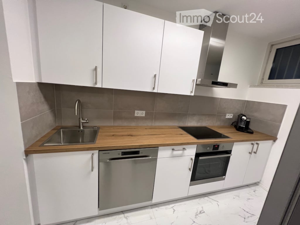 Modern kitchen with white cabinets, wooden countertop, stainless steel appliances including a sink, stove, oven, and dishwasher, and a range hood above the stove.