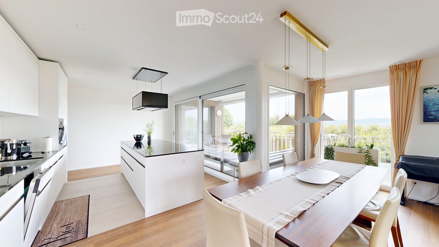 Modern open-plan kitchen and dining area with white cabinets, a central island, pendant lights, and large windows overlooking a balcony.