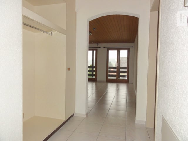 Empty hallway with tiled floor, white walls, wooden ceiling, and double doors leading outside.