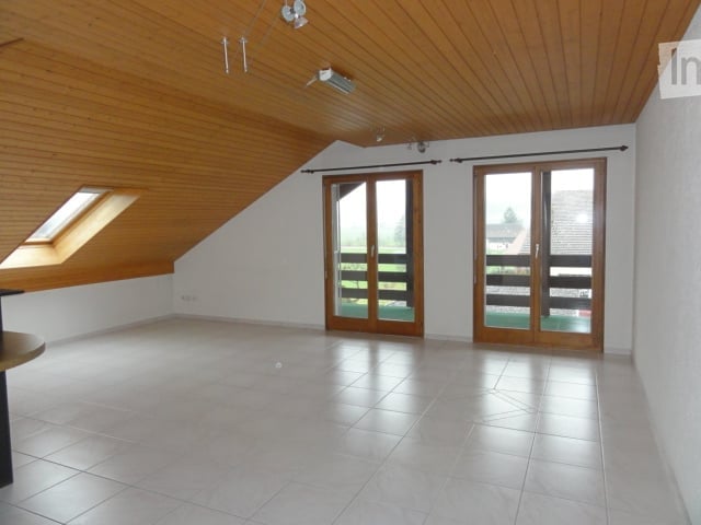 Bright, empty attic room with wooden ceiling, white walls, large skylight, and two sliding glass doors leading to a balcony.