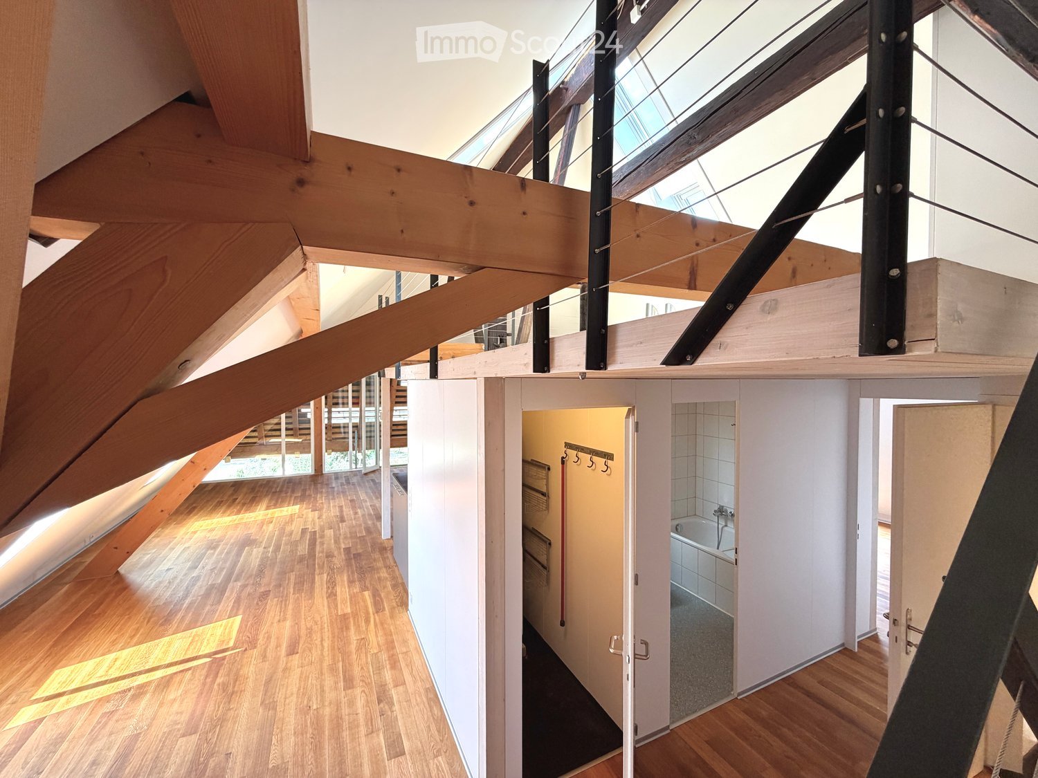 Open hallway with wooden flooring, white walls, and visible rooms including a bathroom with a bathtub and a closet with hanging space.