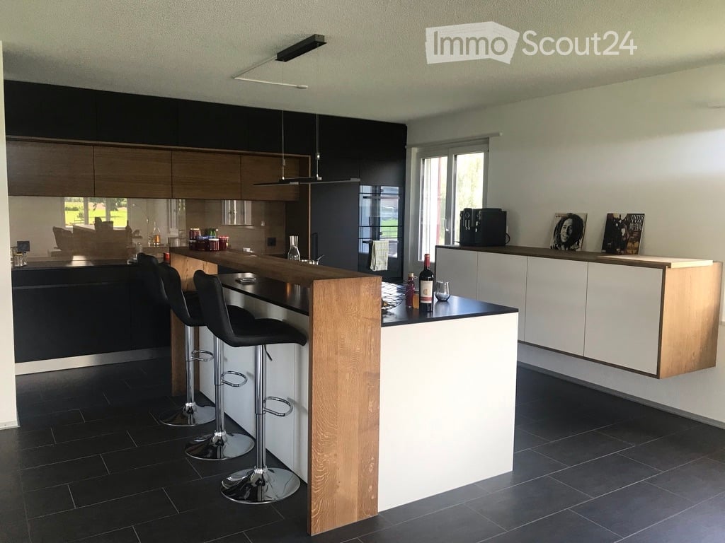 Modern kitchen with dark cabinets, wooden island, black stools, and pendant lights.
