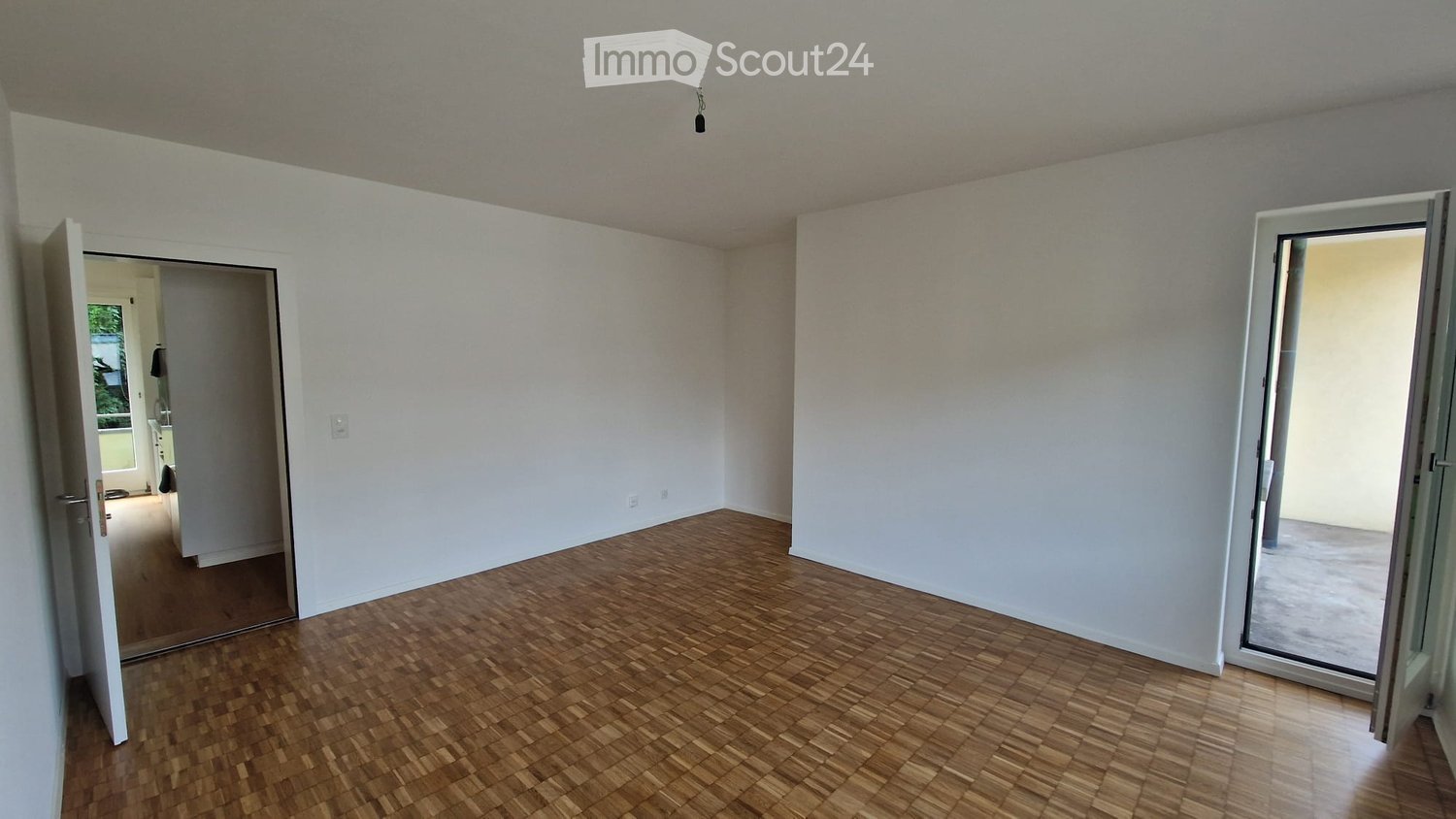 Empty room with wooden flooring, white walls, and large sliding glass doors leading to a balcony or outdoor area.