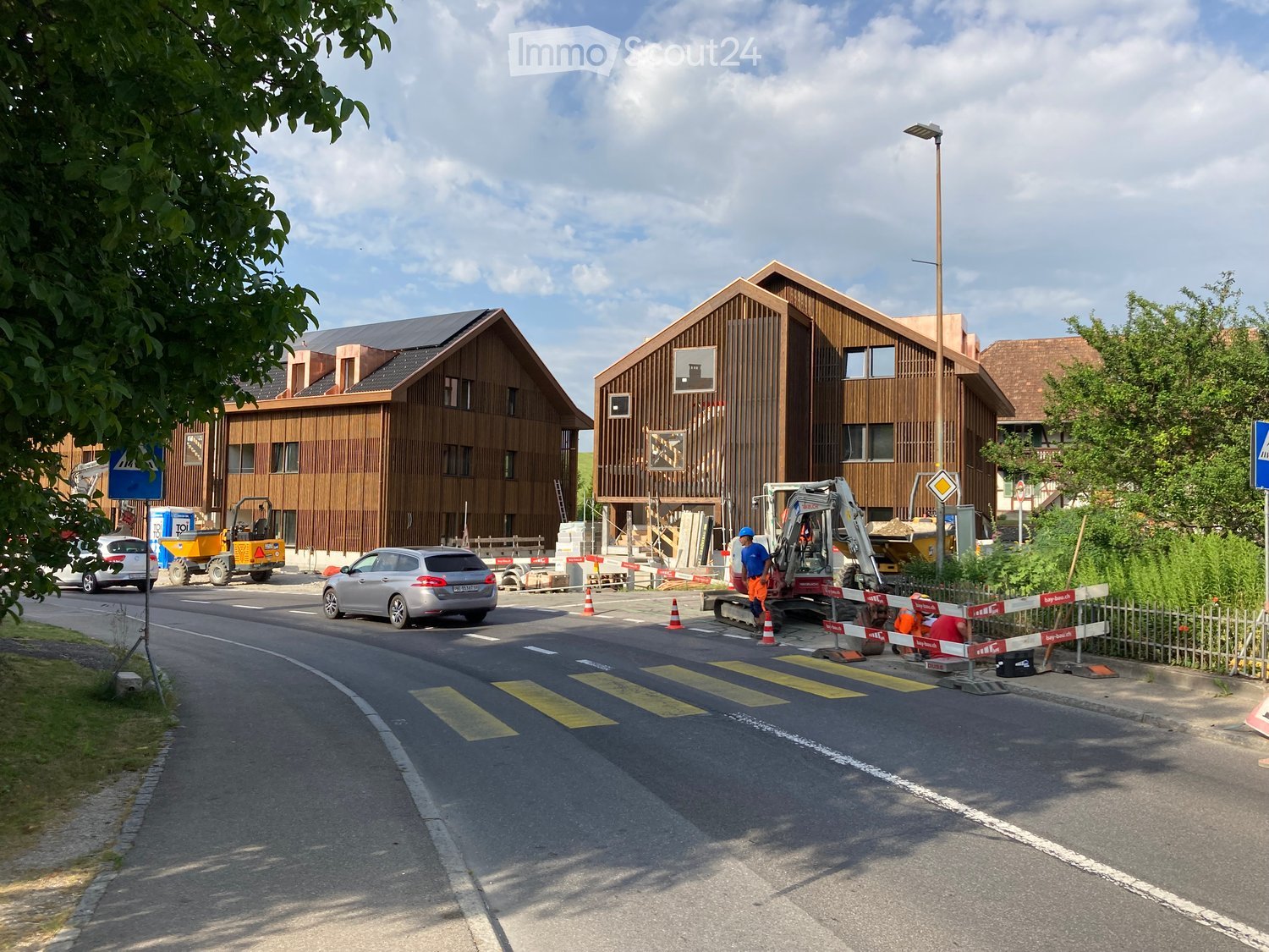 Modern wooden residential buildings under construction with visible construction equipment and barriers.