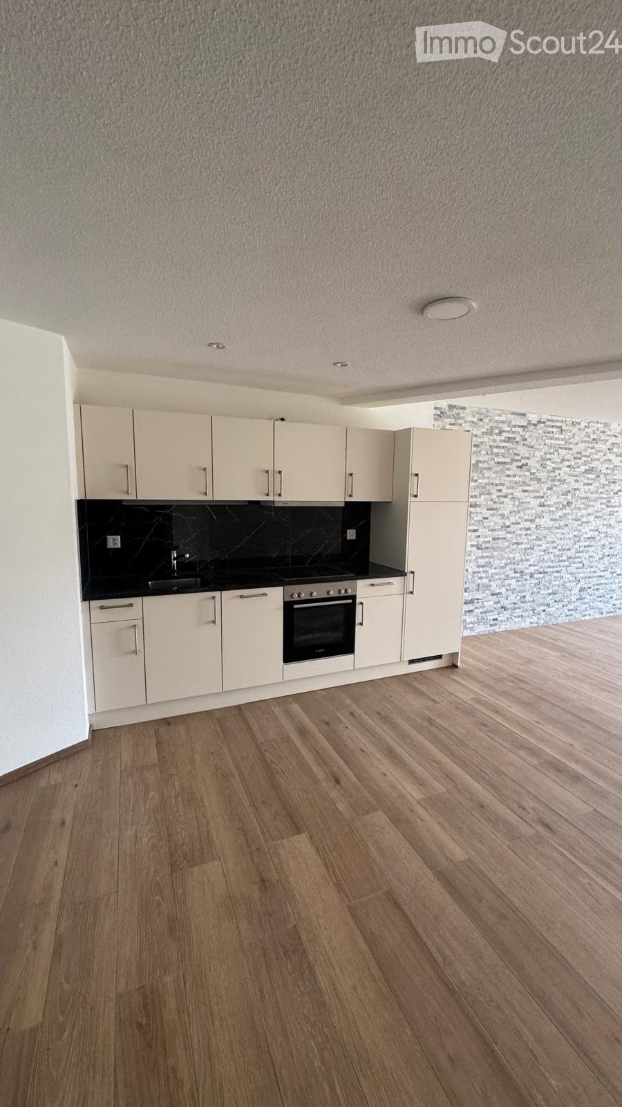 Modern kitchen with light-colored cabinets, a black countertop, and a wooden floor. The space includes a sink, an oven, and ample cabinet storage.