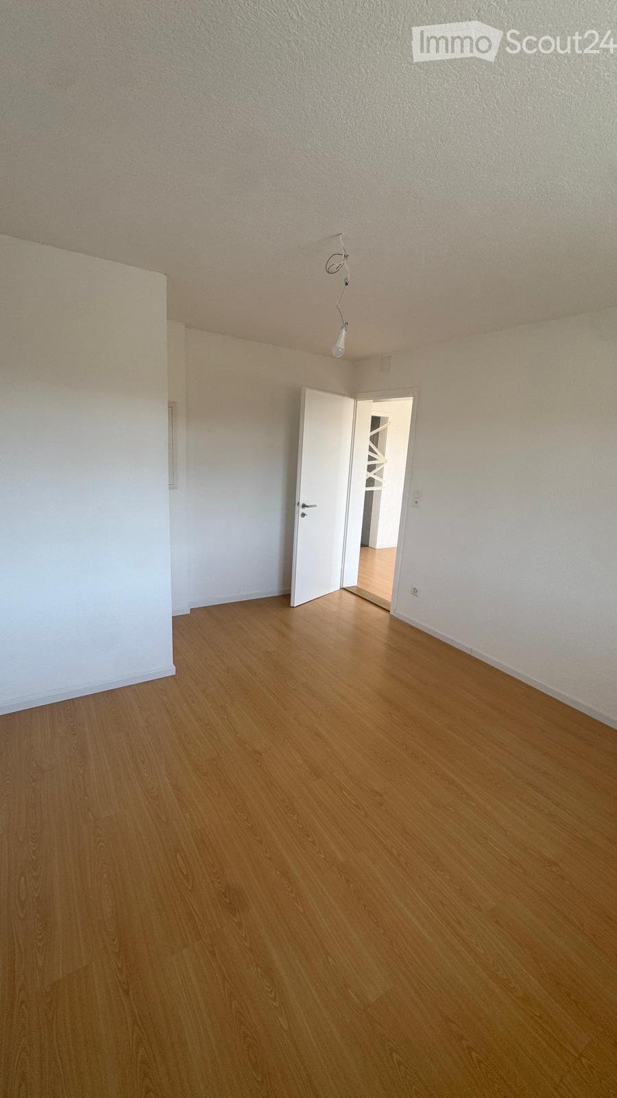 Empty room with wooden flooring, white walls, and a single open door leading to another room.