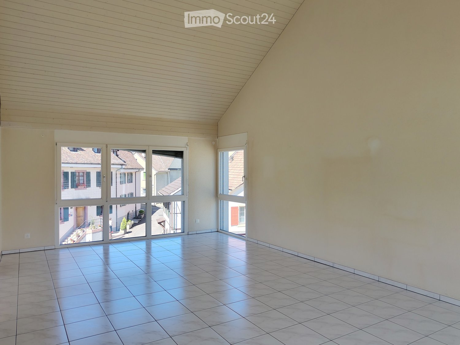 Empty room with tiled floor, large windows, and wooden ceiling beams.