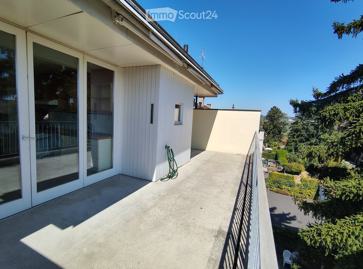 Balcony with concrete floor, glass sliding doors, metal railing, and a view of greenery and trees.
