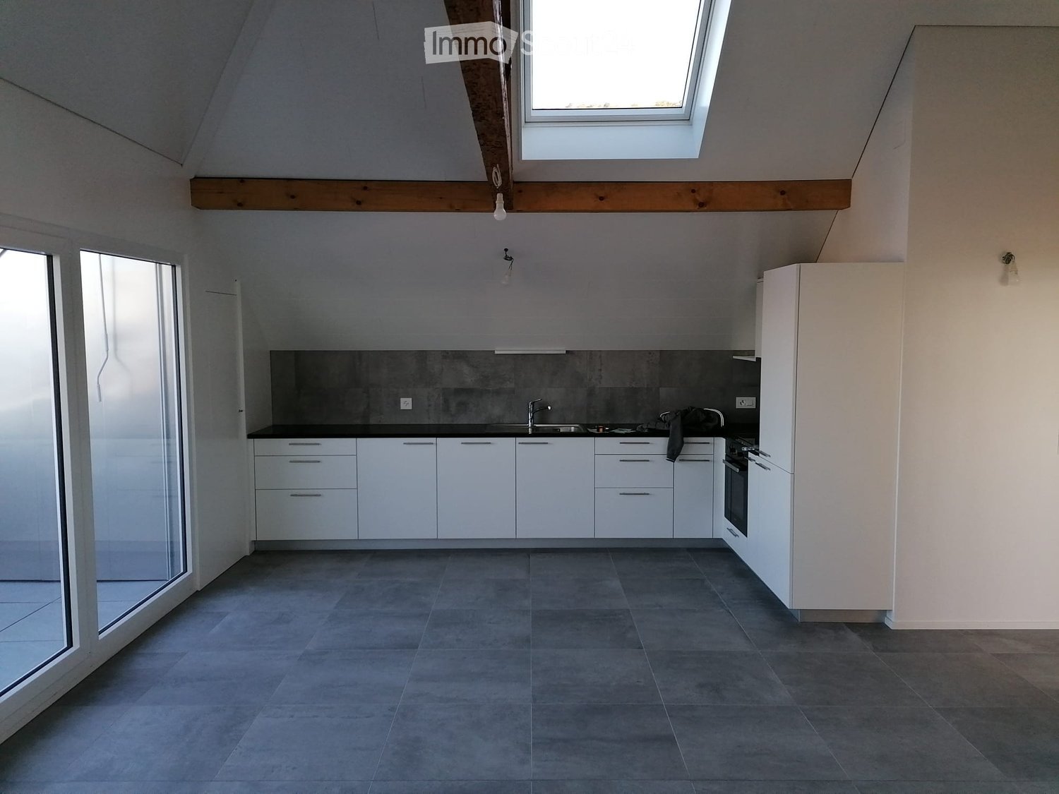 Modern kitchen with white cabinets, dark countertops, and a grey tiled floor. Features a large window and a skylight above.