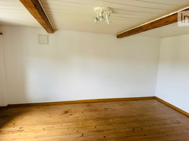 Completely empty room with white walls, wooden floor, and exposed wooden beams on the ceiling. No furniture or equipment.