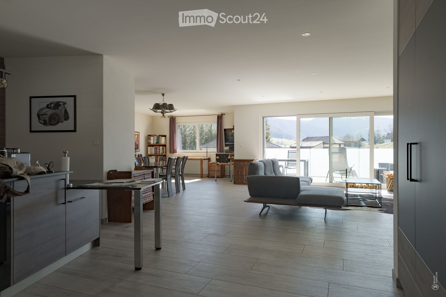 Open-plan living and dining area with modern furniture, large windows, and a view of the landscape.