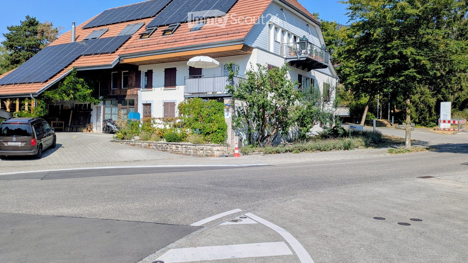Two-story house with red-tiled roof, solar panels, white walls, multiple windows, and a balcony with outdoor furniture.