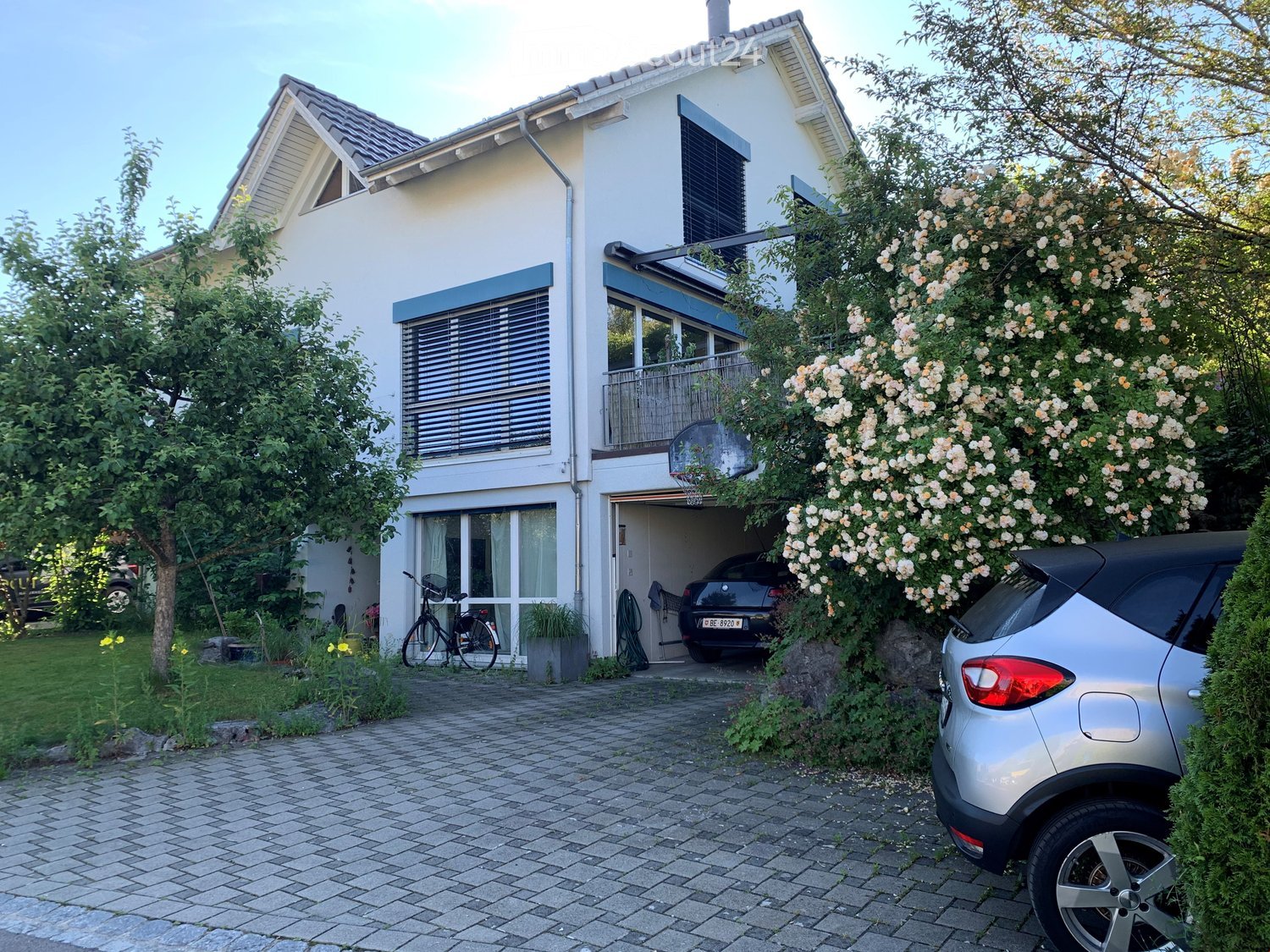 Two-story house with white exterior, garage, balcony, and driveway with parked cars.