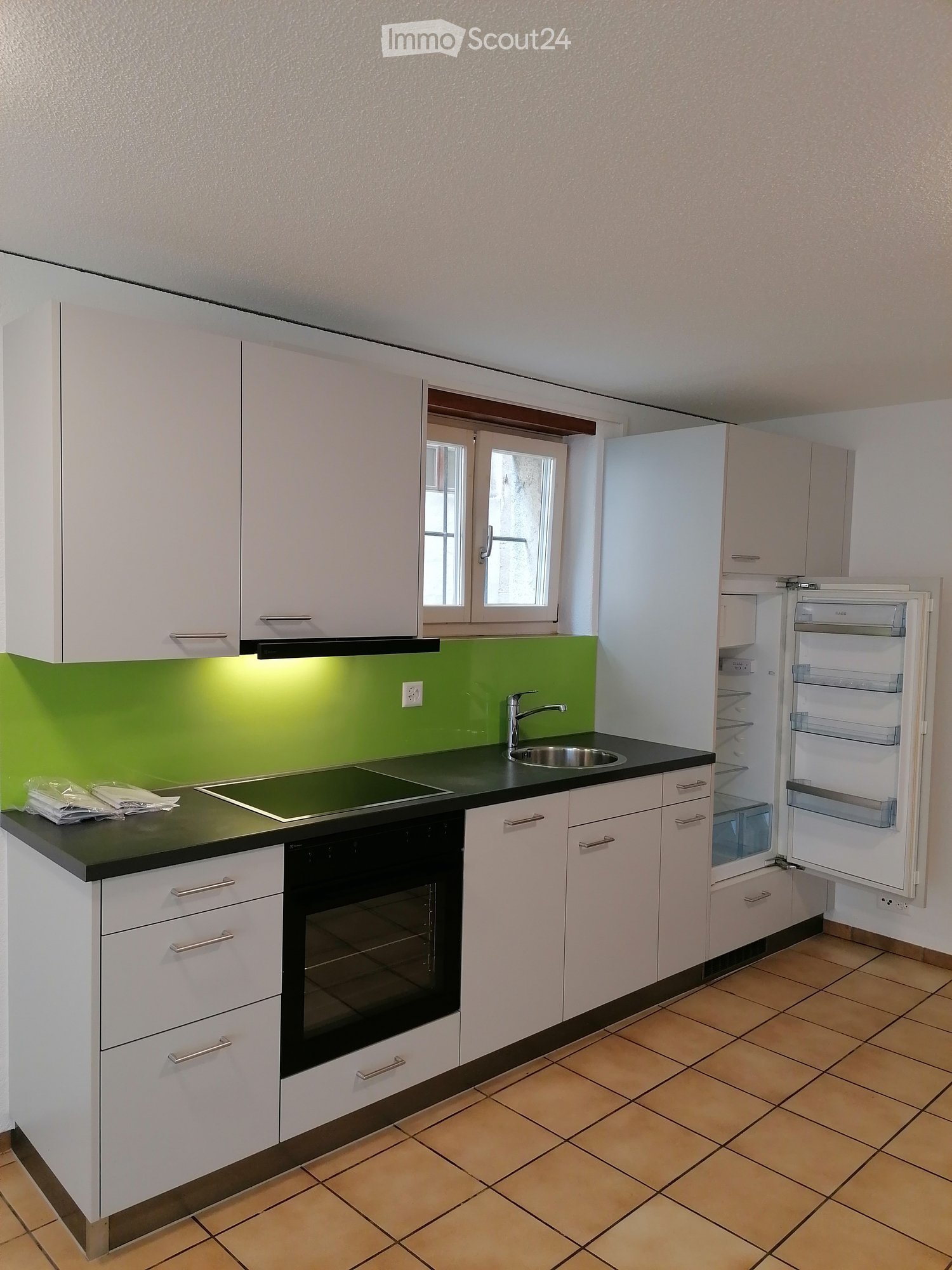 Modern kitchen with white cabinets, black countertops, induction cooktop, sink, and open refrigerator.