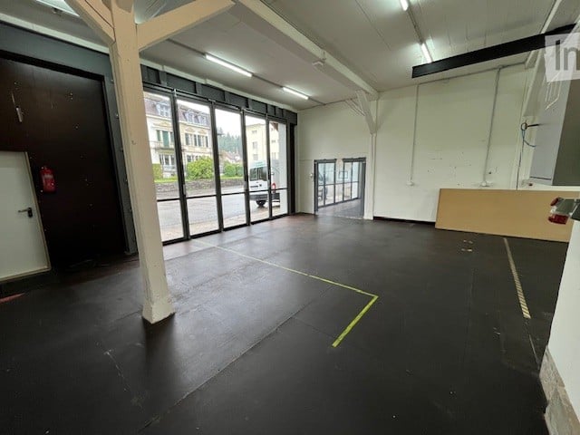 Empty warehouse, black floor, white walls, glass windows, emergency exit, fire extinguisher, white ceiling lights, two doors