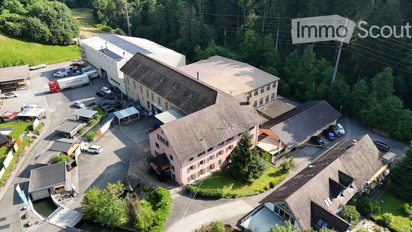 Aerial view of a multi-building industrial or commercial complex with parking areas, surrounded by greenery.
