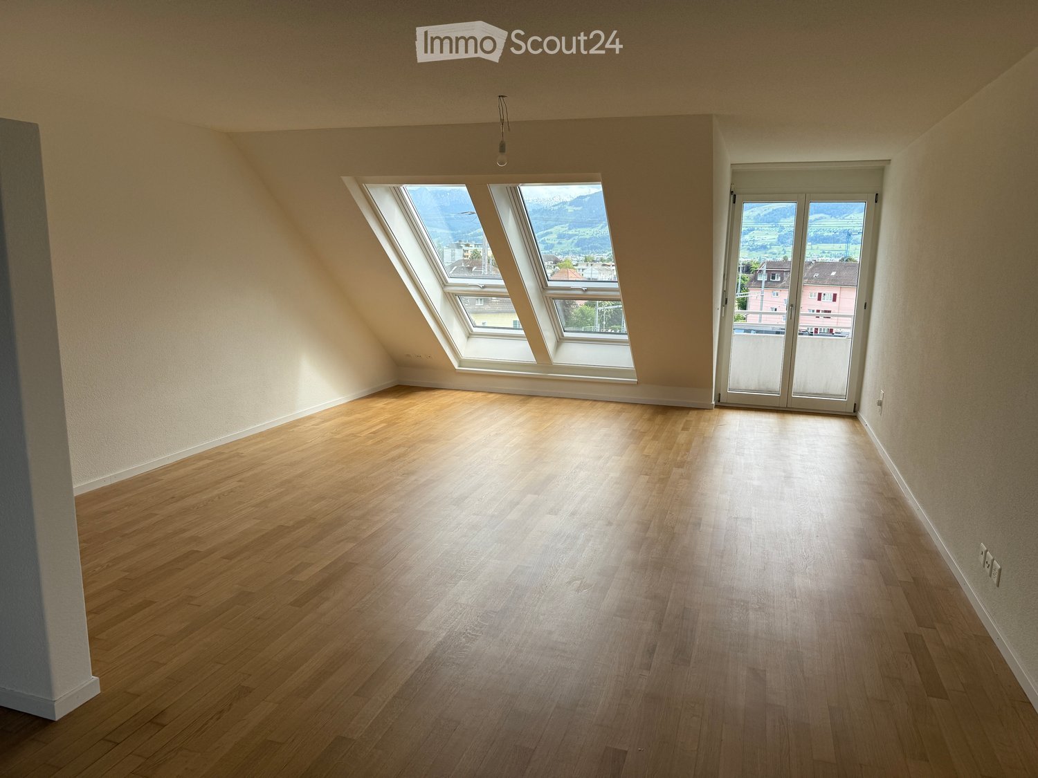 Empty room with wooden flooring, large windows, and a sliding glass door leading to a balcony.