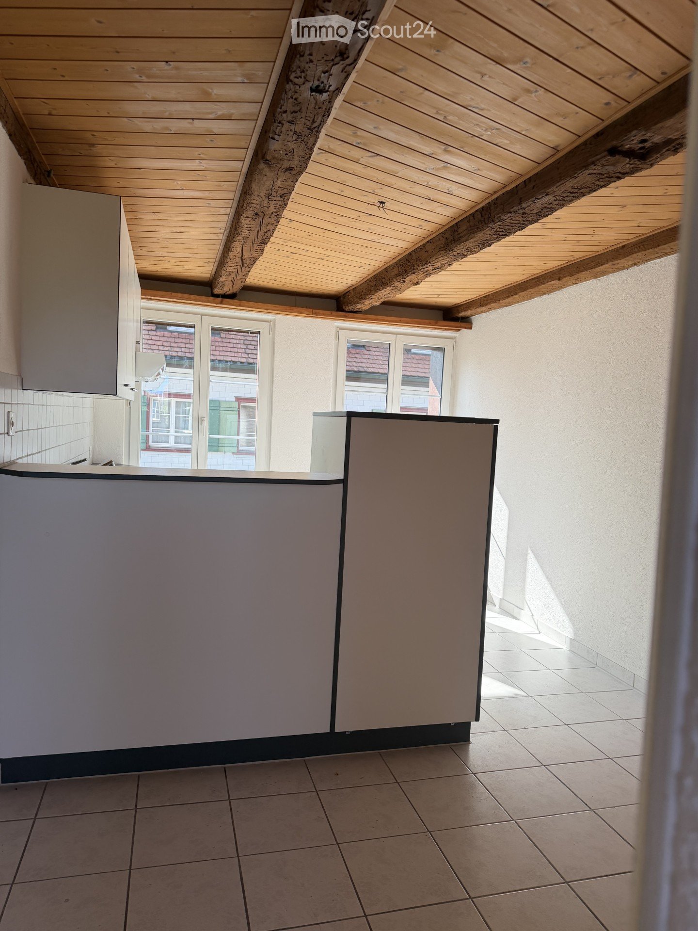 Empty kitchen with modern cabinets, tiled floor, and large windows offering a view of the street.