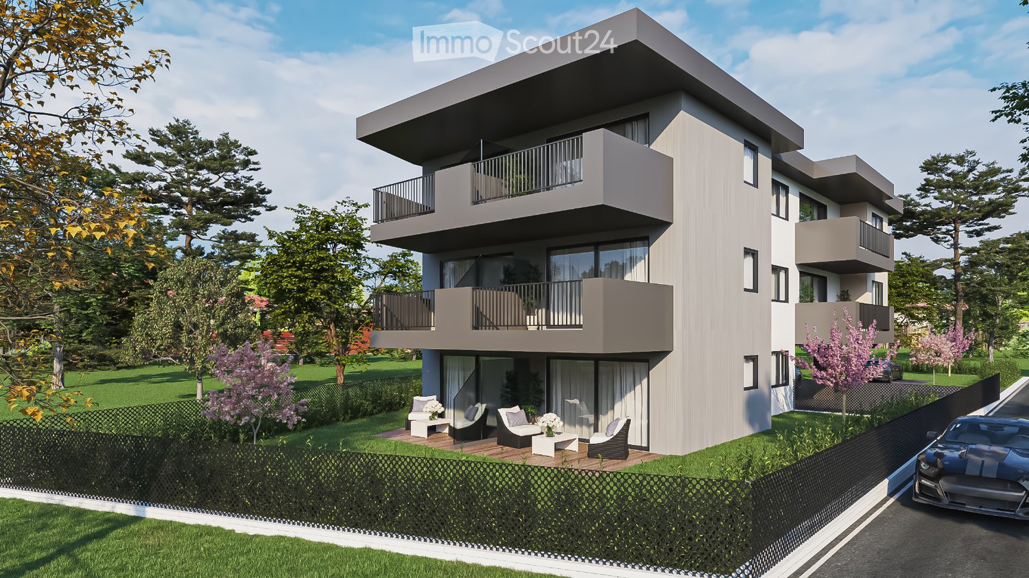 Modern two-story house with balconies, surrounded by greenery and a small patio area with outdoor furniture.