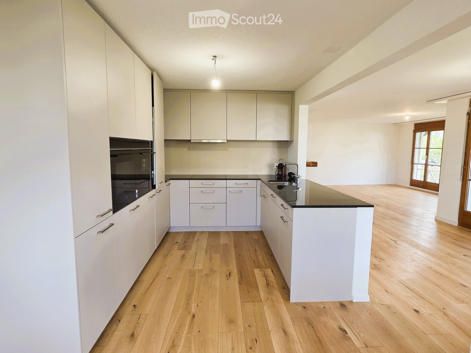 Modern kitchen with white cabinets, black countertops, and wooden floors.