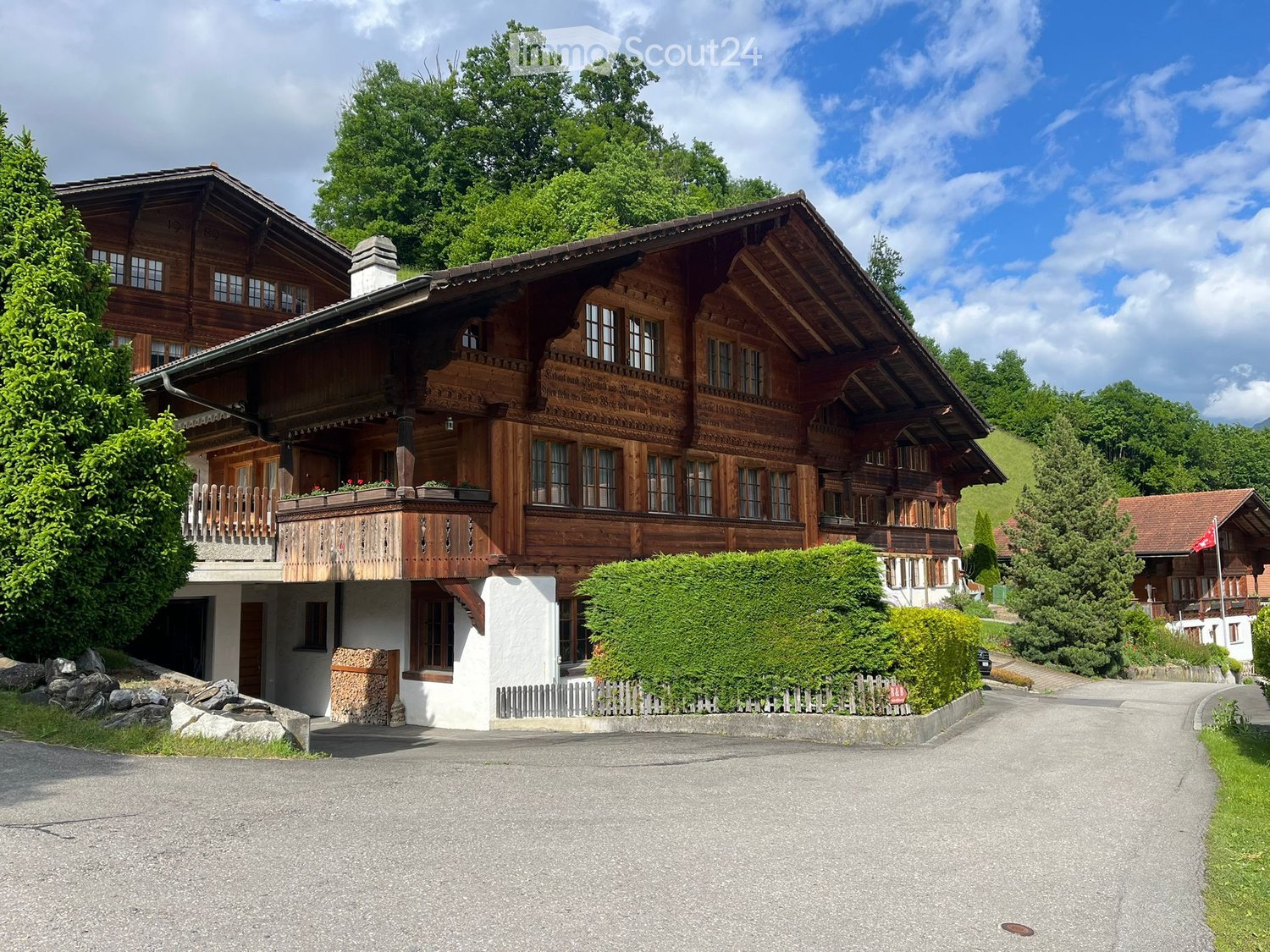 Traditional wooden house with a large balcony, multiple windows, and a well-maintained garden.