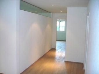 Empty hallway with wooden flooring and white walls, leading to a door at the end.