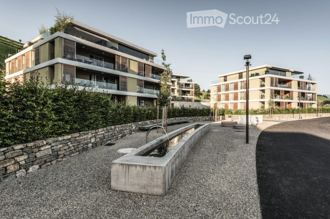 Modern multi-story residential buildings with balconies and contemporary design, surrounded by greenery and a paved walkway.