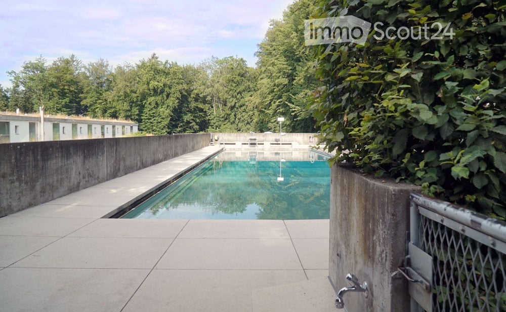 Outdoor swimming pool area with concrete walls, tiled deck, and surrounding greenery.