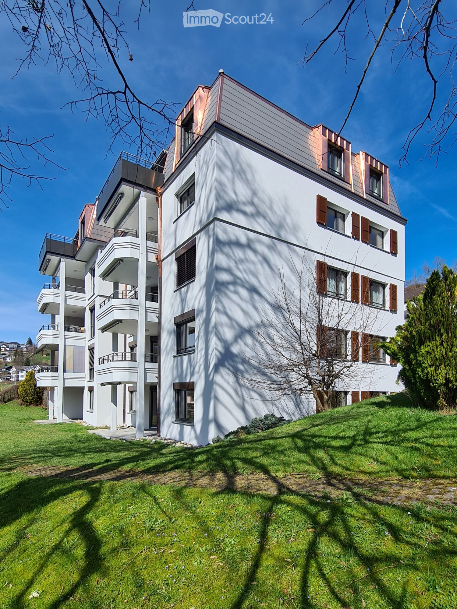 Multi-story apartment building, white exterior, multiple balconies, brown shutters, situated on a hill, surrounded by greenery
