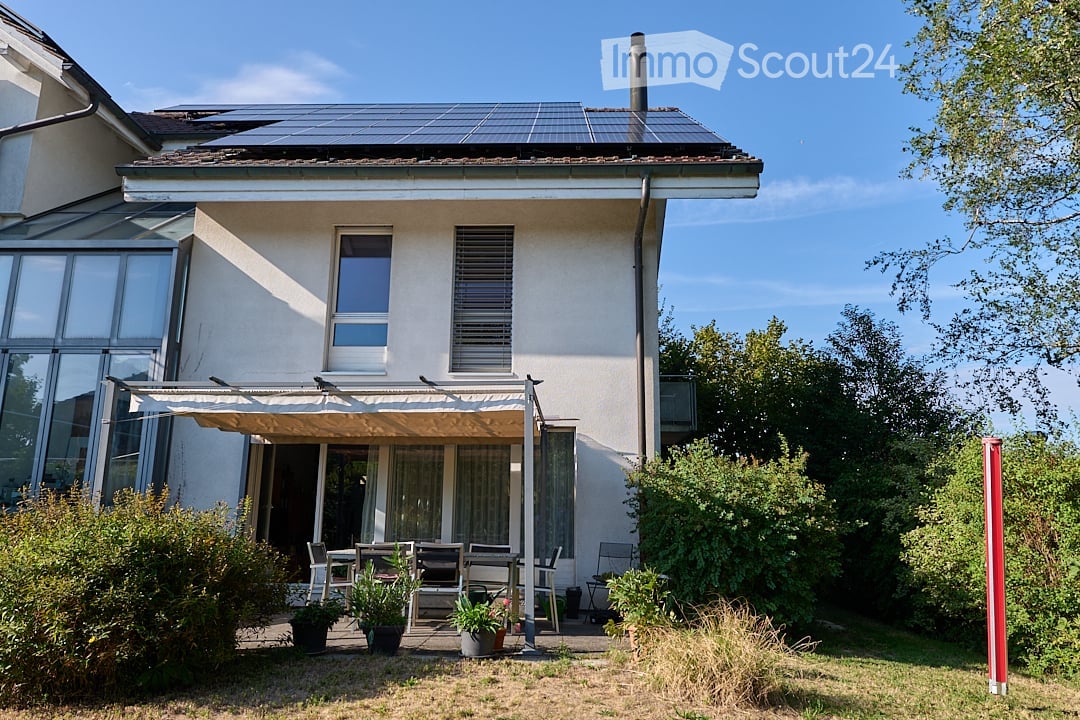 Two-story house with solar panels on the roof, large windows, and a covered patio area with outdoor furniture.