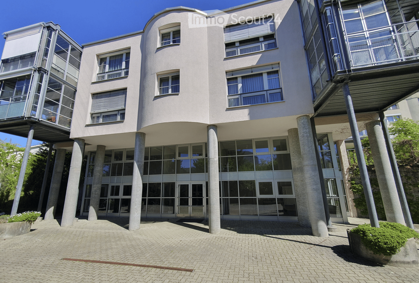 Modern building with a curved facade, large glass windows, and a raised ground floor supported by concrete pillars.