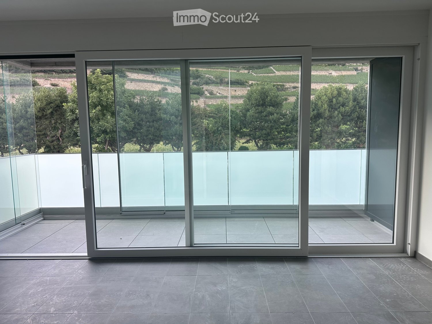 Empty room with large sliding glass doors leading to a balcony, tiled floor, and modern white frame.
