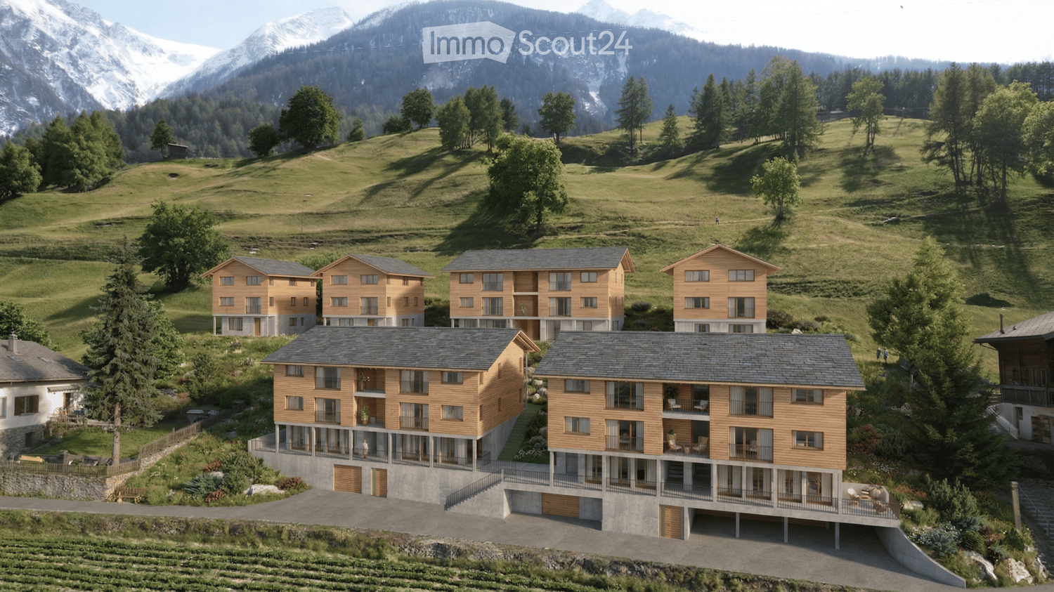 A cluster of modern wooden houses with balconies and large windows, set in a lush green valley with mountains in the background.