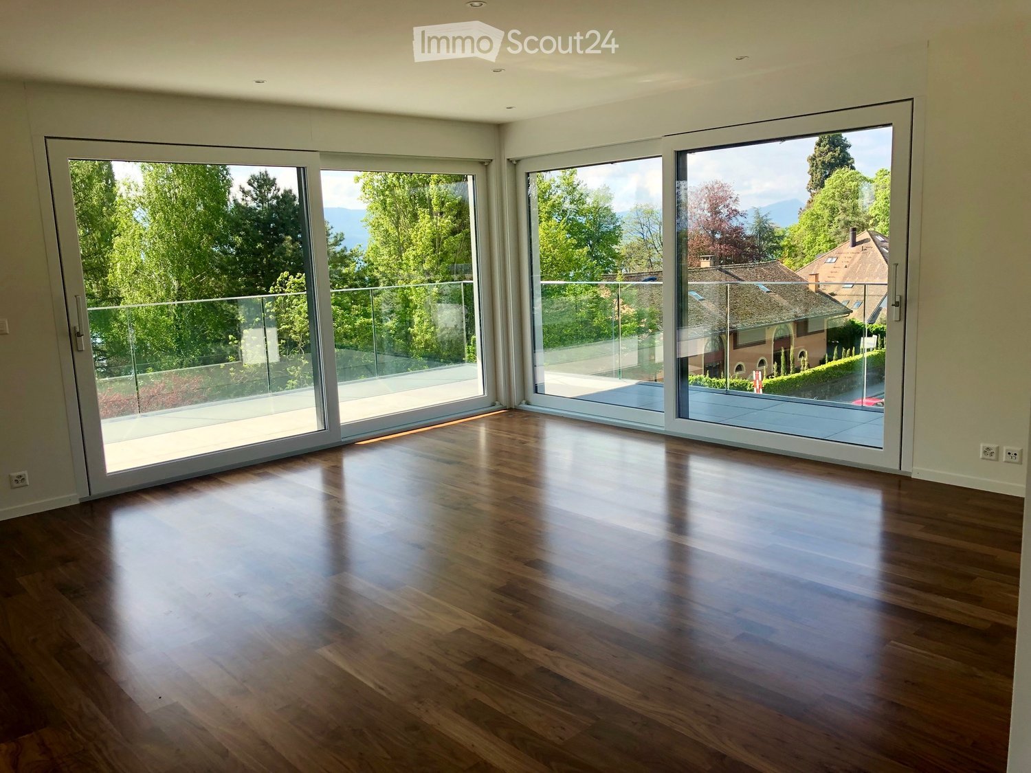 Empty room with wooden flooring and large sliding glass doors leading to a balcony with a scenic view of trees and mountains.