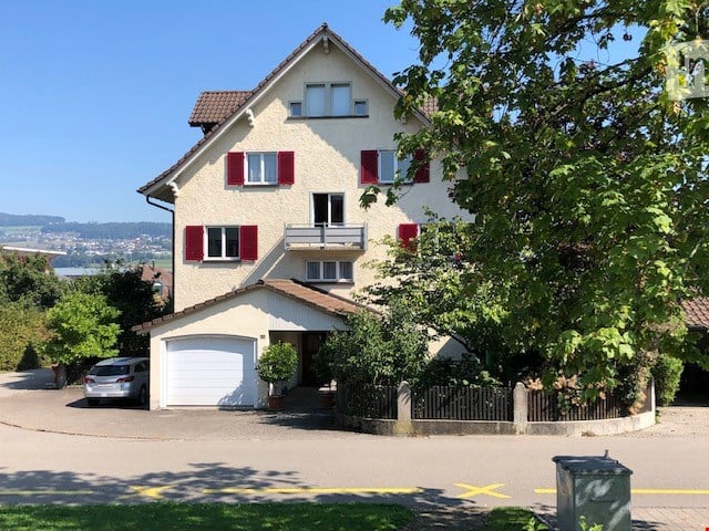 Two-story house with red shutters, white windows, garage, and driveway with a parked car.