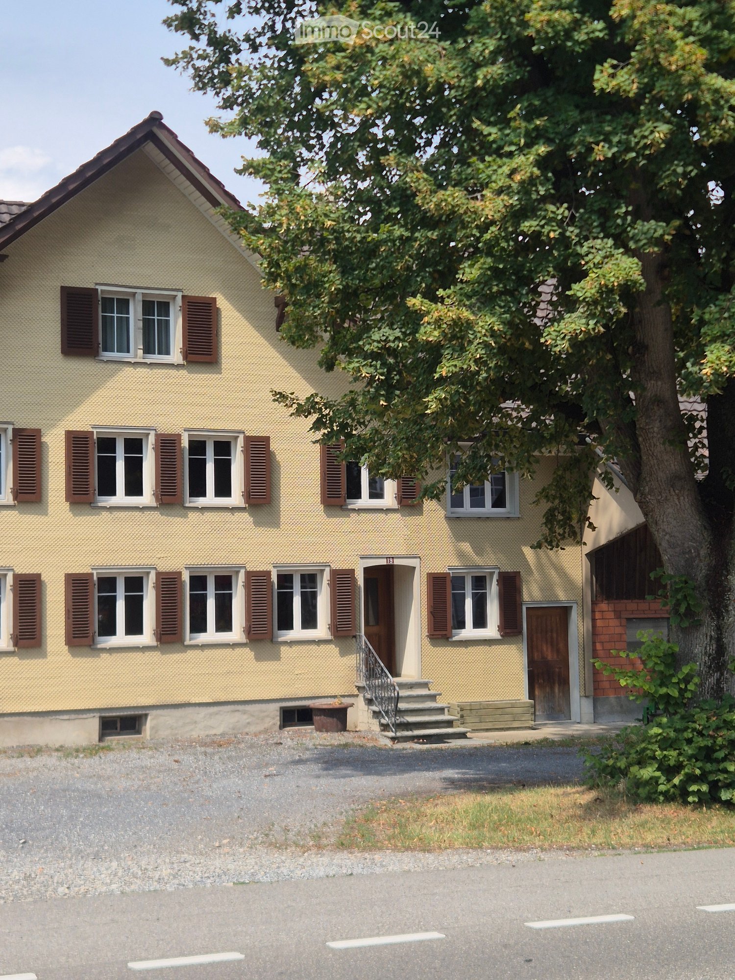 Two-story yellow house with multiple windows, wooden shutters, and a small staircase leading to the entrance.