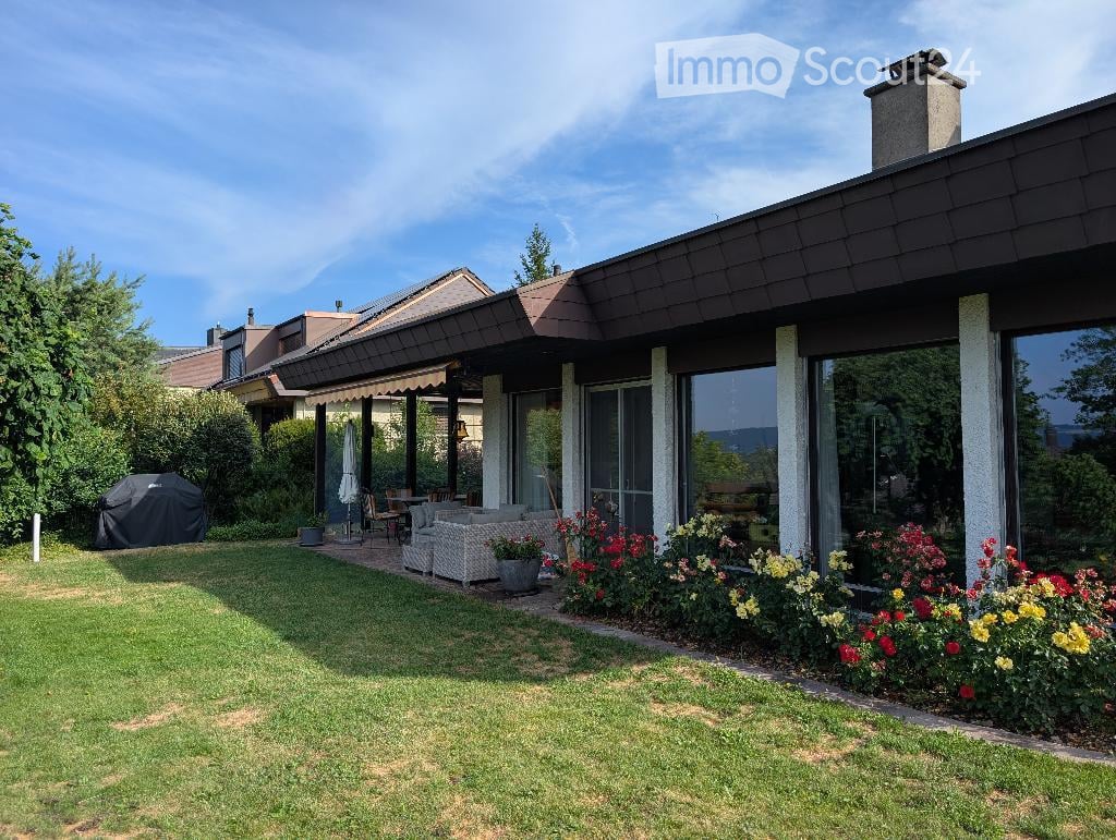 Well-maintained garden with a lawn, patio seating area, covered outdoor space, and colorful flower beds.
