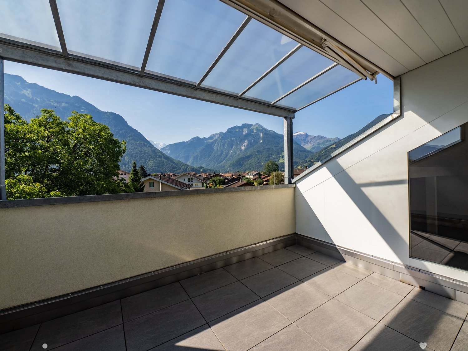 Balcony with tiled floor, glass roof, and scenic mountain view.