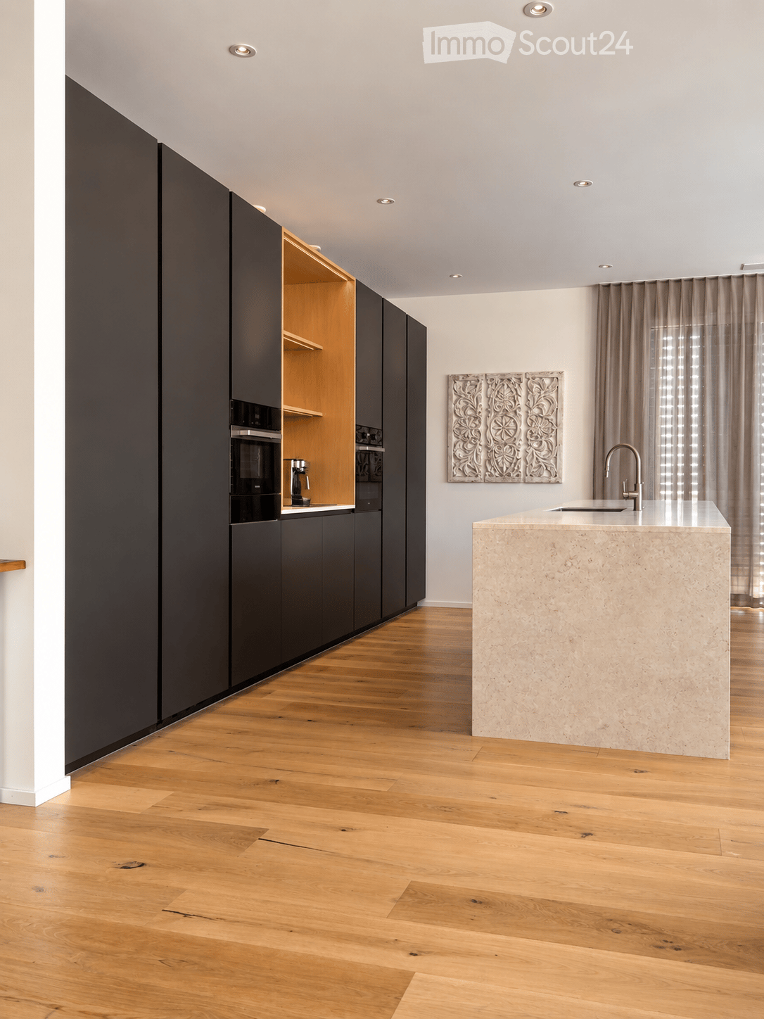 Modern kitchen with dark cabinets, light wooden floor, central island with marble countertop, and a sink with a modern faucet.